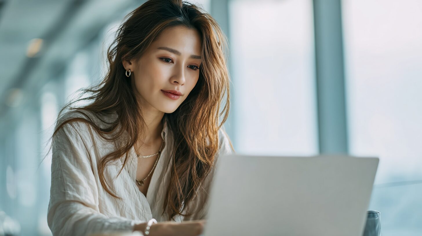 窓辺でノートパソコンを前にほほえむ女性のイメージ